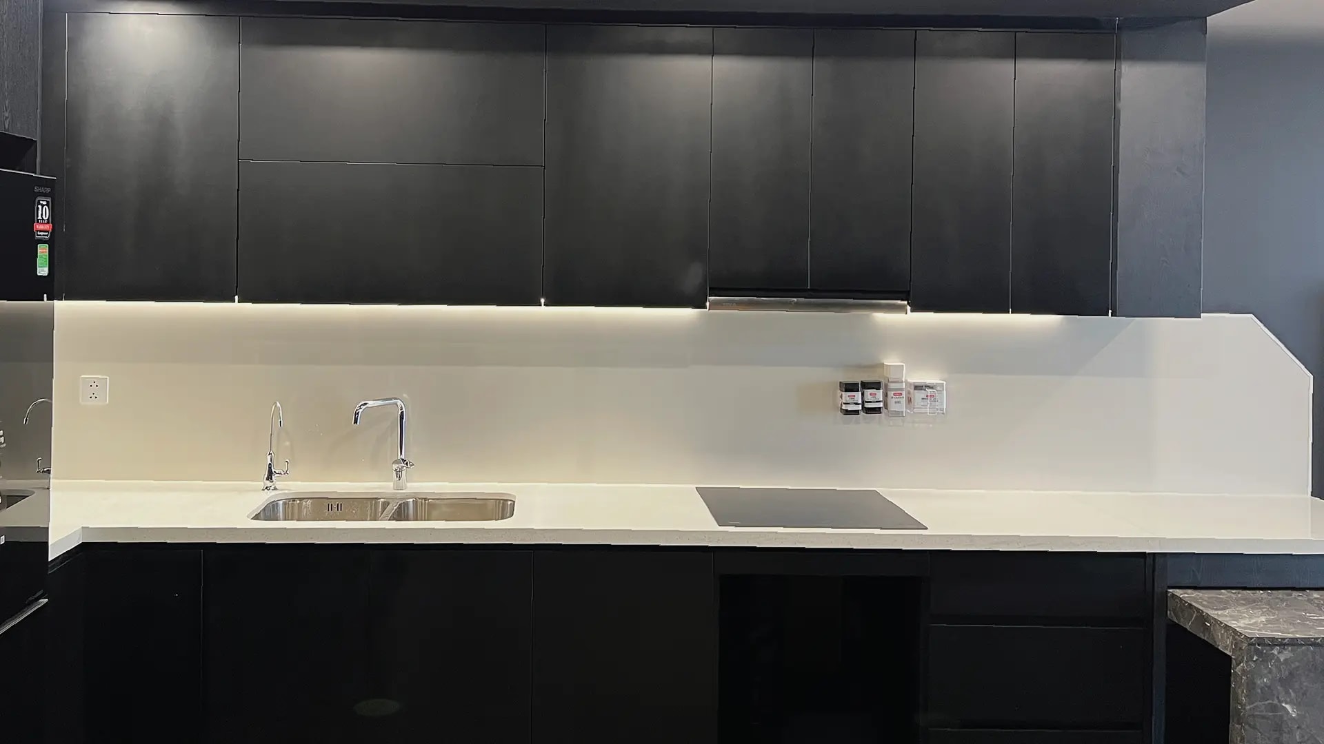 Bếp căn hộ ốp tấm thép tráng men sứ trắng Kurashi sau khi thi công xong, tường liền mạch từ bồn rửa tới bếp từ